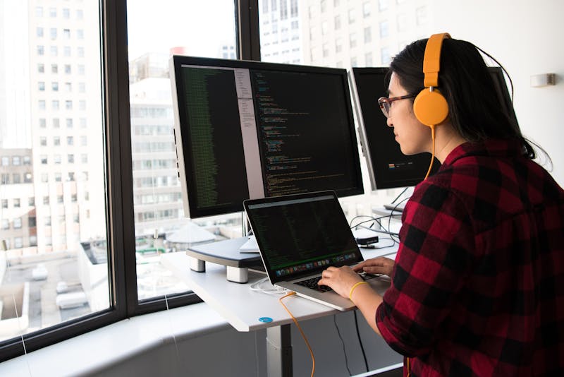 Desarrolladora trabajando en múltiples pantallas con código, representando scripting avanzado